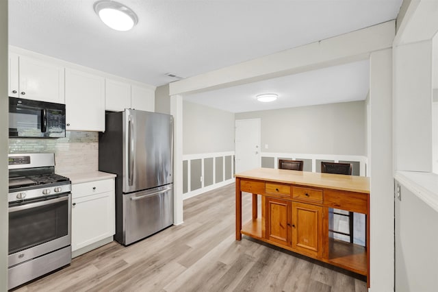 kitchen with stainless steel appliances, light wood-type flooring, white cabinets, decorative backsplash, and wainscoting