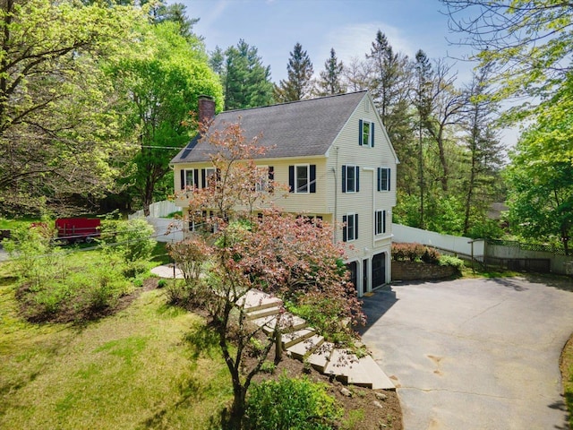 view of property exterior featuring a chimney, an attached garage, driveway, fence, and roof with shingles