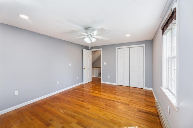 unfurnished bedroom featuring a baseboard heating unit, baseboards, light wood-style floors, recessed lighting, and a closet