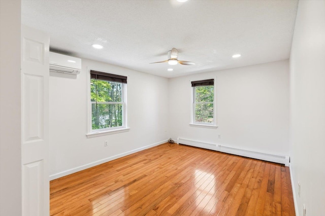 spare room featuring baseboard heating, a wall mounted air conditioner, plenty of natural light, light wood-style floors, and recessed lighting