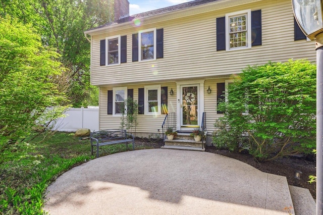 colonial home with a chimney, fence, and a patio