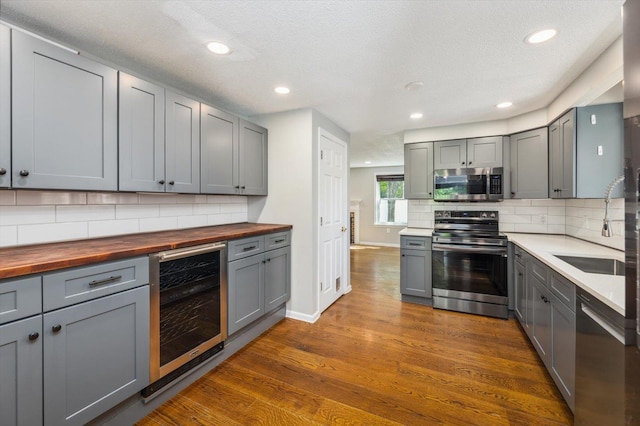 kitchen featuring appliances with stainless steel finishes, wood counters, beverage cooler, gray cabinetry, and a sink