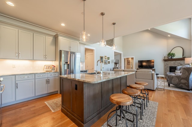kitchen with stainless steel fridge with ice dispenser, a sink, a fireplace, light wood-style floors, and light stone counters
