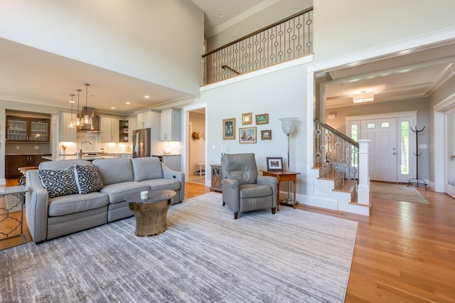 living room featuring light wood-type flooring, stairs, crown molding, and baseboards