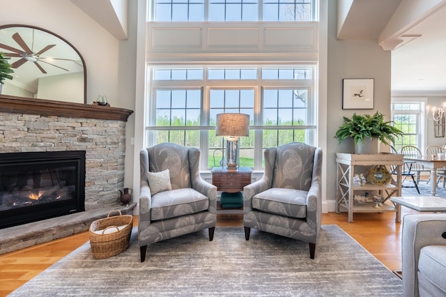 living area featuring wood finished floors, ceiling fan, a stone fireplace, and a chandelier