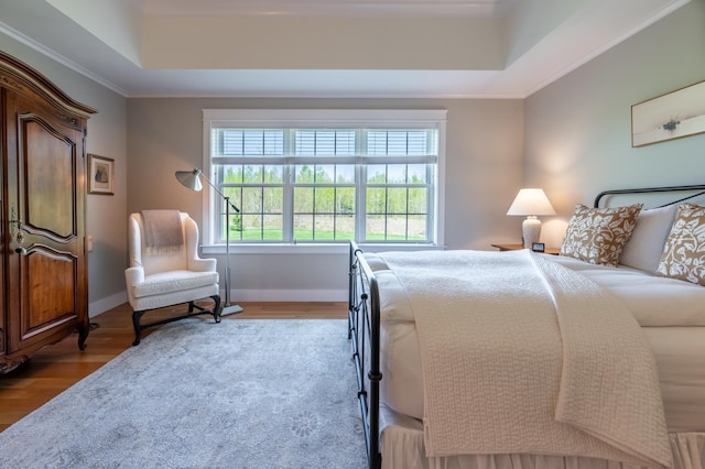 bedroom featuring a tray ceiling, wood finished floors, crown molding, and baseboards