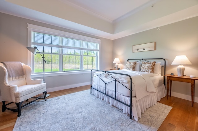bedroom featuring a raised ceiling, baseboards, wood finished floors, and crown molding
