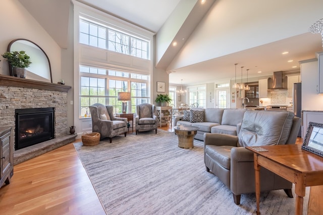 living room featuring plenty of natural light, a chandelier, a fireplace, light wood-style flooring, and high vaulted ceiling