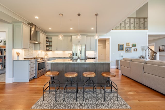 kitchen featuring appliances with stainless steel finishes, wall chimney exhaust hood, open shelves, a breakfast bar area, and light wood-type flooring