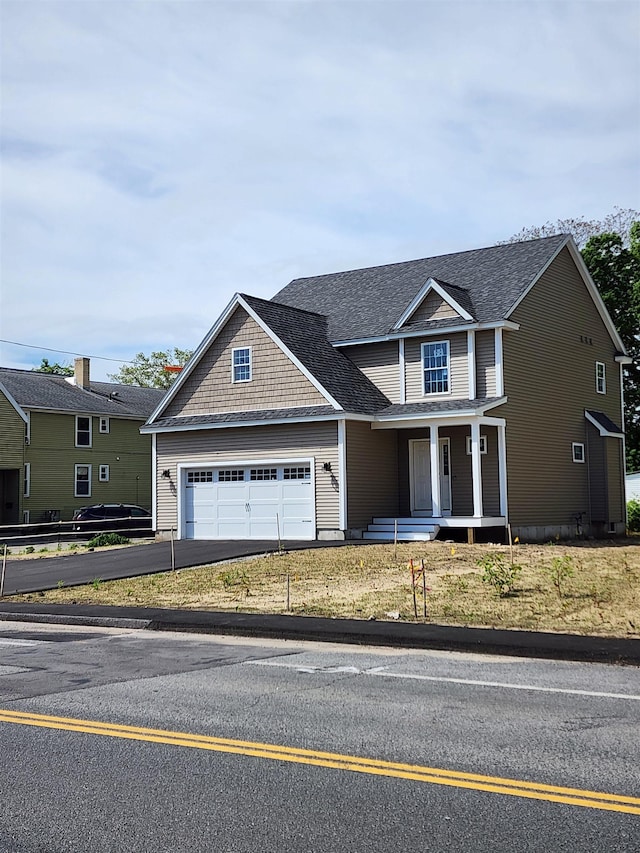 traditional-style home with a porch, asphalt driveway, a garage, and a shingled roof