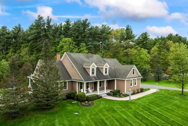 cape cod-style house featuring covered porch, a front lawn, a chimney, and a forest view