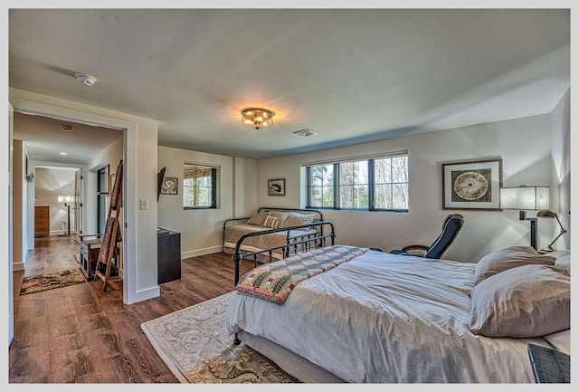 bedroom with multiple windows, dark wood-type flooring, and baseboards