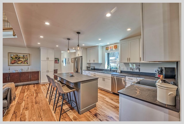 kitchen featuring stainless steel appliances, dark countertops, a sink, a breakfast bar area, and recessed lighting