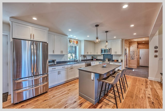 kitchen featuring appliances with stainless steel finishes, dark countertops, a sink, light wood finished floors, and recessed lighting