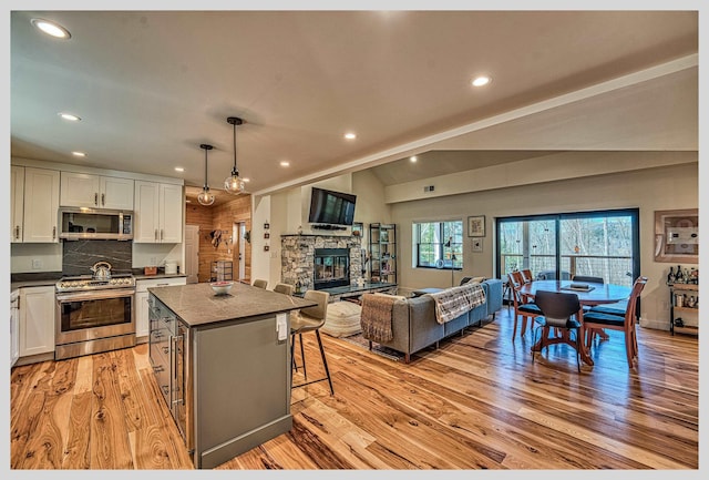 kitchen with appliances with stainless steel finishes, dark countertops, a center island, light wood-style flooring, and a fireplace
