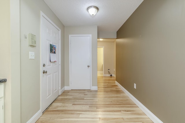 corridor featuring light wood finished floors, a textured ceiling, and baseboards