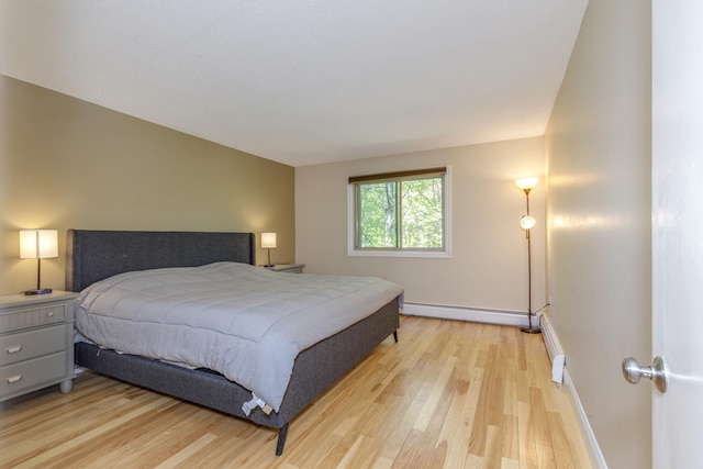 bedroom featuring a baseboard heating unit, light wood finished floors, and baseboards