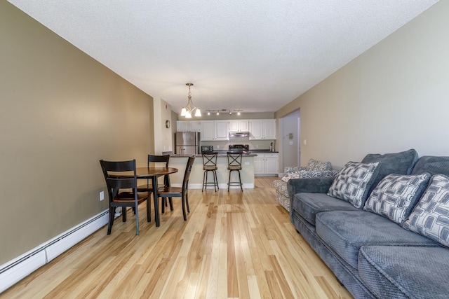 living room featuring a baseboard heating unit, light wood-style flooring, a chandelier, baseboards, and rail lighting