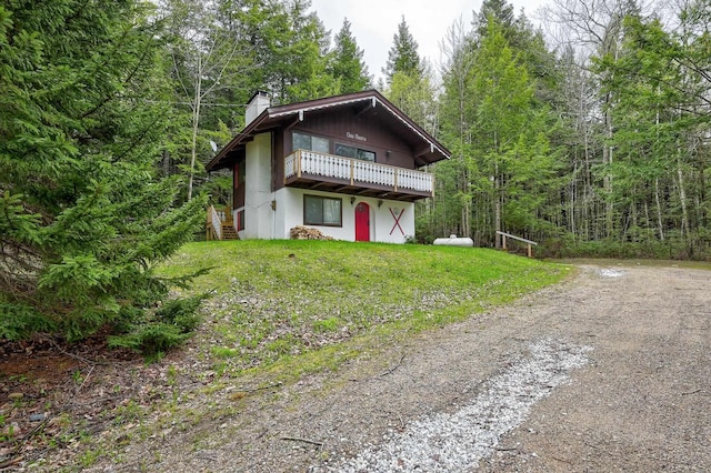 view of front of house featuring a chimney, a deck, a front yard, dirt driveway, and a view of trees