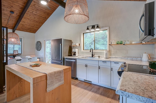 kitchen featuring stainless steel appliances, a sink, light wood-type flooring, beam ceiling, and plenty of natural light
