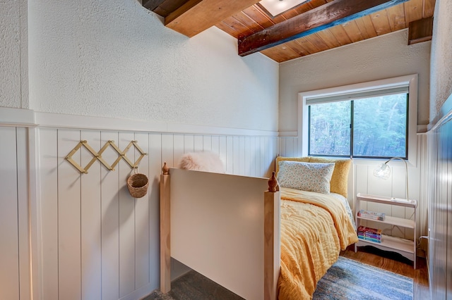 bedroom with beamed ceiling, wooden ceiling, wainscoting, a textured wall, and wood finished floors
