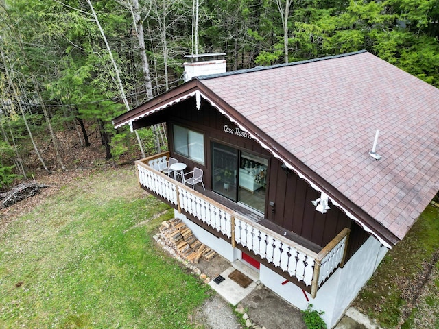 view of front of property featuring a view of trees, a chimney, roof with shingles, a front yard, and board and batten siding