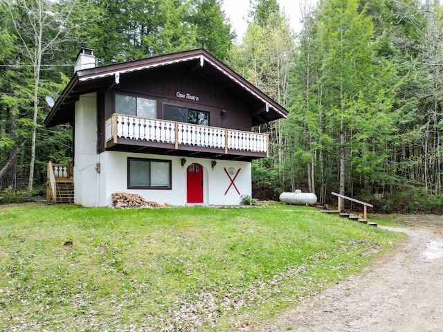 chalet / cabin with a chimney, a front lawn, a wooden deck, a forest view, and stucco siding