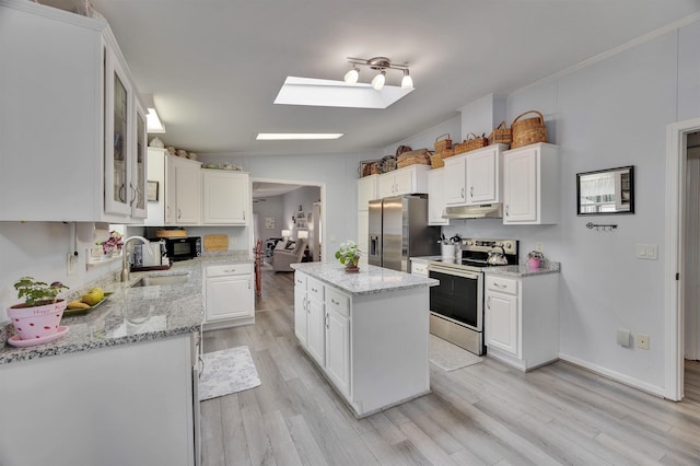 kitchen featuring appliances with stainless steel finishes, a skylight, under cabinet range hood, a sink, and white cabinets