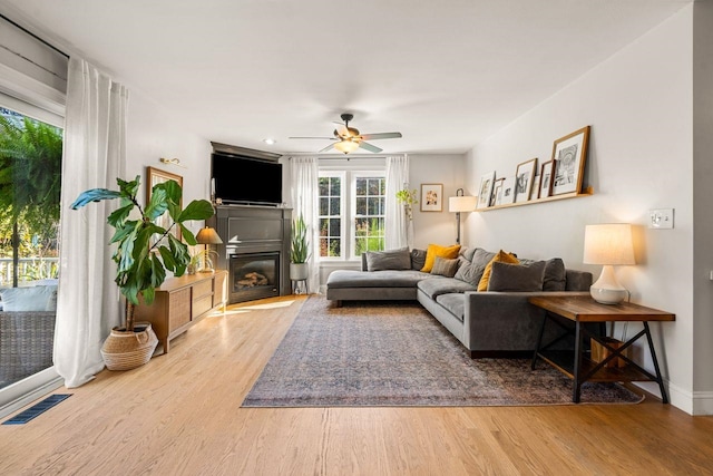 living room with wood finished floors, ceiling fan, a glass covered fireplace, and baseboards