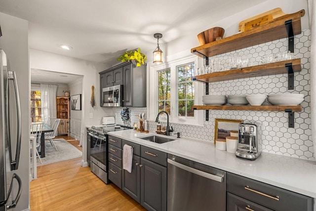 kitchen featuring stainless steel appliances, a sink, open shelves, decorative backsplash, and light wood-style floors