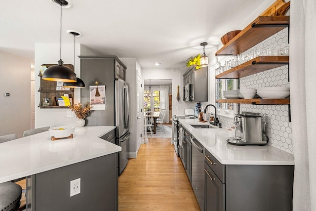 kitchen featuring open shelves, appliances with stainless steel finishes, a sink, a peninsula, and light wood-type flooring