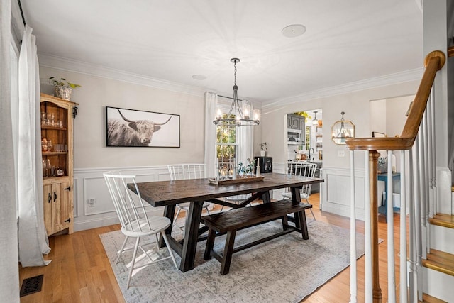 dining area with a chandelier, light wood-style flooring, crown molding, stairs, and wainscoting
