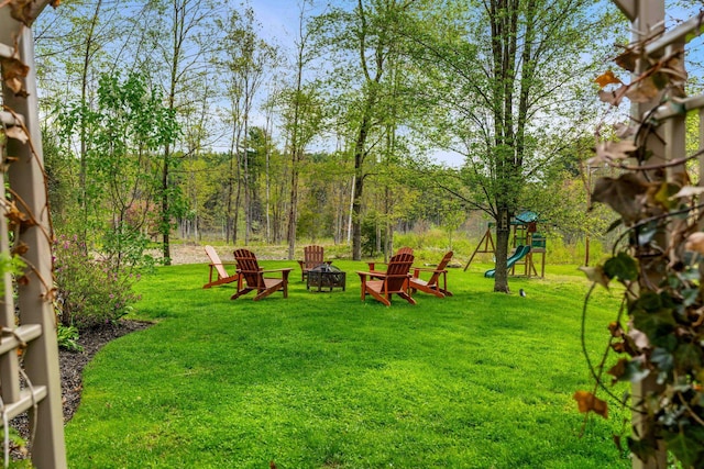 view of green lawn featuring a fire pit and a playground