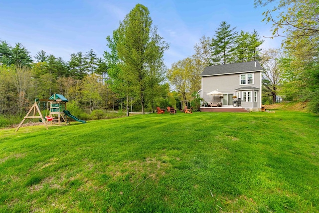 view of grassy yard with a wooden deck and a playground