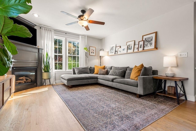 living area featuring ceiling fan, wood finished floors, a glass covered fireplace, baseboards, and recessed lighting