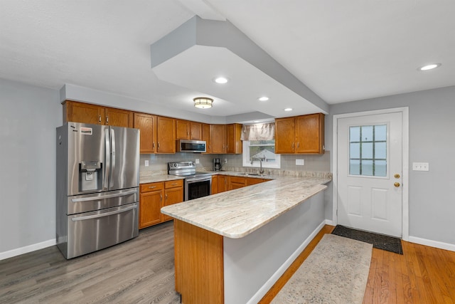 kitchen featuring stainless steel appliances, a peninsula, baseboards, brown cabinetry, and recessed lighting