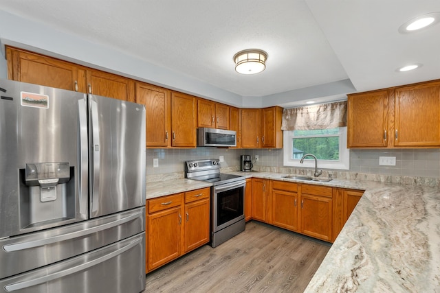 kitchen with stainless steel appliances, a sink, light wood finished floors, and brown cabinets