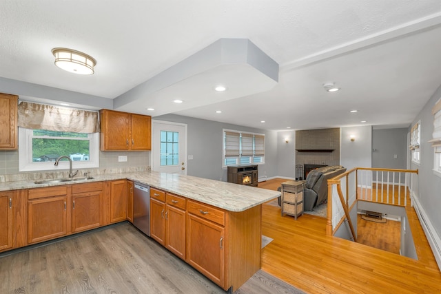 kitchen featuring a brick fireplace, a sink, dishwasher, light wood-type flooring, and a peninsula