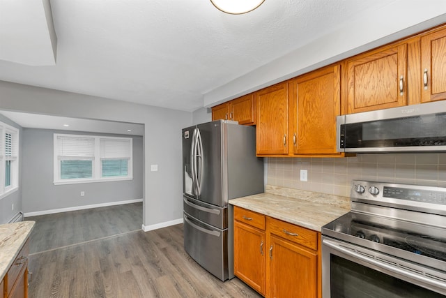 kitchen featuring stainless steel appliances, decorative backsplash, brown cabinets, and dark wood finished floors