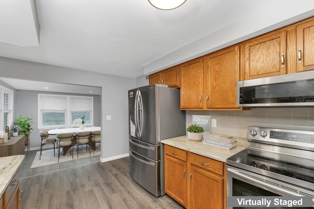 kitchen featuring appliances with stainless steel finishes, tasteful backsplash, brown cabinetry, and wood finished floors