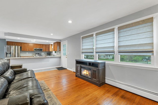 living area with a baseboard radiator, light wood-type flooring, recessed lighting, and baseboards