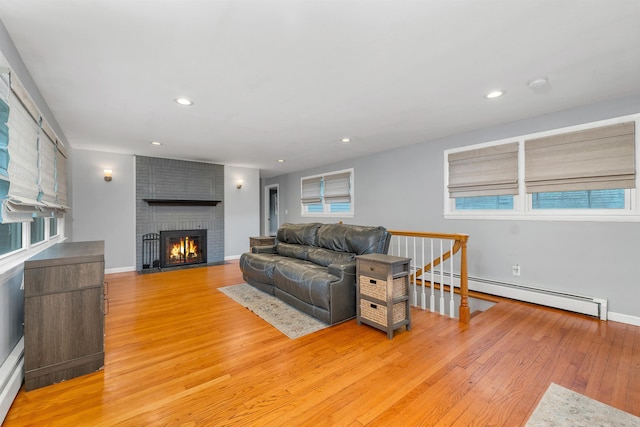 living area featuring a baseboard radiator, light wood-style flooring, a brick fireplace, baseboards, and a baseboard heating unit