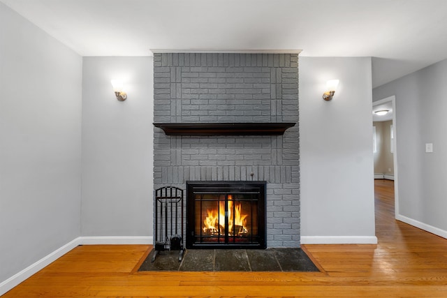 detailed view of a brick fireplace, wood finished floors, and baseboards