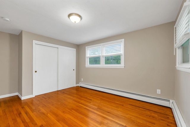 unfurnished bedroom with baseboard heating, light wood-type flooring, a closet, and baseboards
