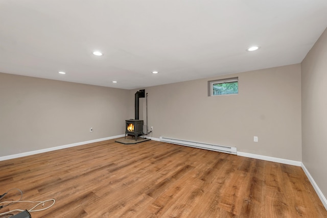 basement featuring baseboard heating, a wood stove, light wood-style floors, baseboards, and recessed lighting
