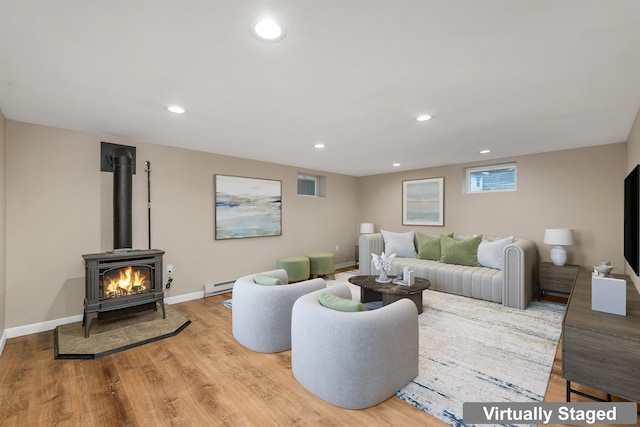 living area featuring light wood-style floors, recessed lighting, baseboard heating, a wood stove, and baseboards