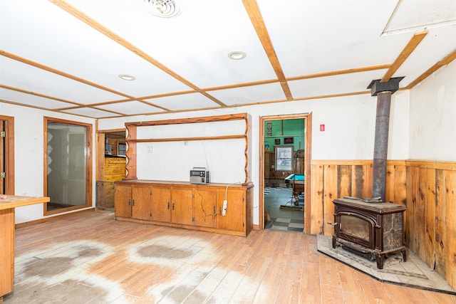 living room featuring a wood stove, light wood-style floors, and a wainscoted wall