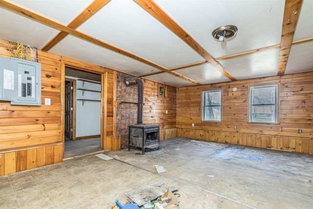 unfurnished living room with electric panel, wooden walls, and a wood stove