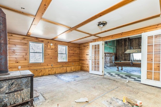 unfurnished living room featuring billiards, french doors, wooden walls, and a wood stove