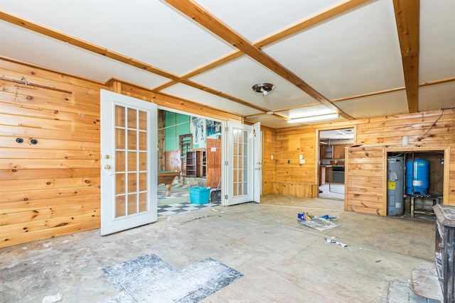 unfurnished living room featuring french doors, wooden walls, and water heater